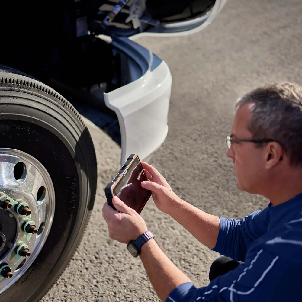 Truck driver conducting vehicle inspection with ISAAC tablet Driver using ISAAC device to record pre-trip inspection by truck wheel